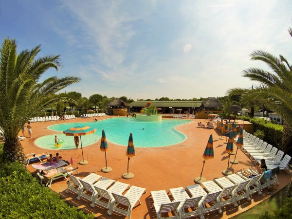 Una piscina circondata da lettini e ombrelloni colorati sotto un cielo soleggiato.