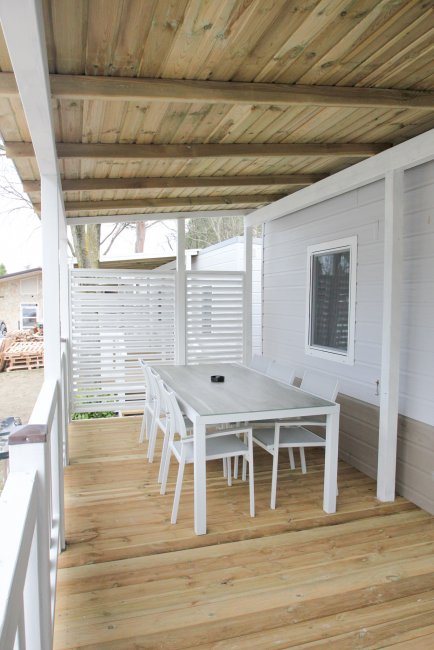 Veranda in legno con tavolo e sedie bianche, pareti chiare e finestre.