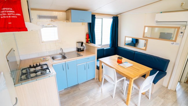 Cucina e area pranzo con tavolo in legno e sedie bianche.