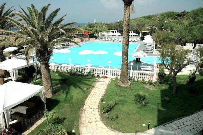 Una piscina circondata da palme e lettini, con vialetti in pietra nel prato.