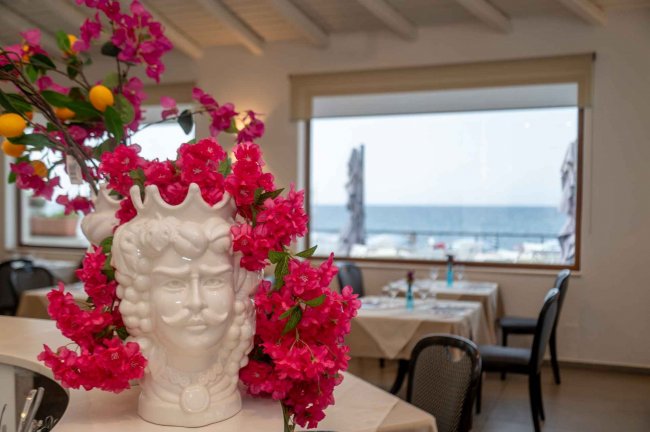 Vaso bianco decorato con fiori rosa, vista mare.