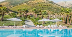 Piscina all'aperto con lettini e ombrelloni, vista su colline verdi.