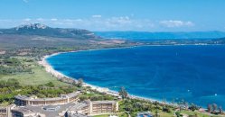 Spiaggia sabbiosa, mare blu intenso, resort e colline sullo sfondo.