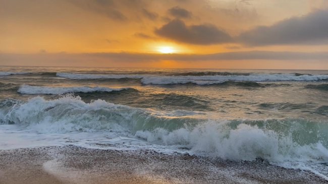 Onde del mare al tramonto con cielo arancione e nuvole.