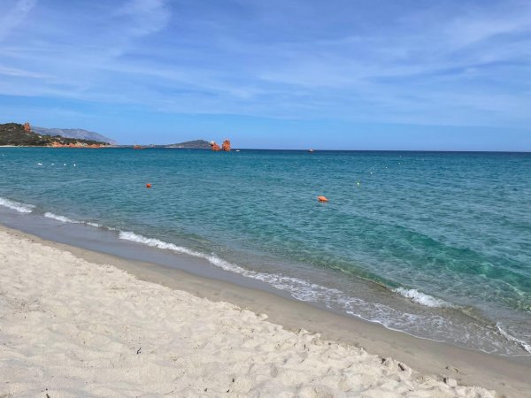 Spiaggia sabbiosa con mare calmo e acqua turchese sotto un cielo azzurro.