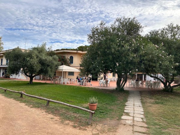 Edificio bianco con veranda, sedie e tavoli all'aperto, circondato da alberi.