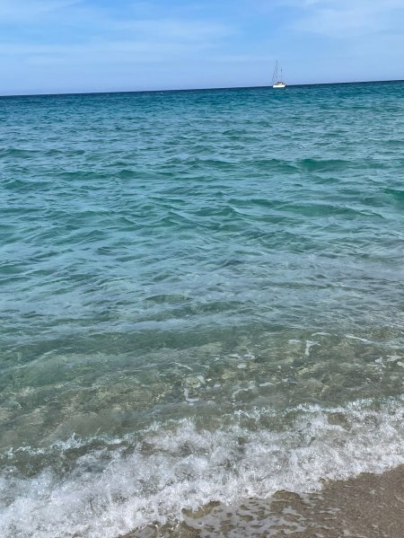 Acqua cristallina di mare con piccole onde, barca all'orizzonte.