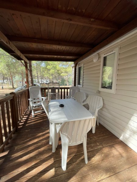 Veranda in legno con tavolo bianco e sedie di plastica.