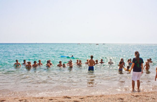 Persone nuotano nel mare vicino alla riva, illuminate dal sole.