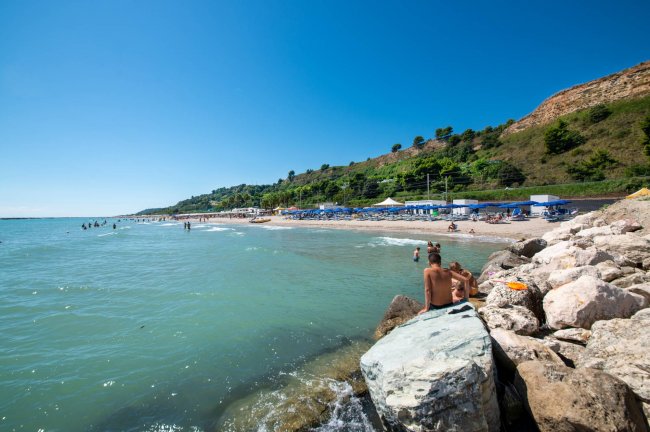 Spiaggia con mare calmo e colline in lontananza.
