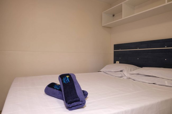 Letto matrimoniale con lenzuola bianche e asciugamani blu piegati sul letto.
