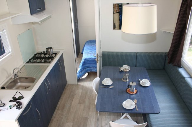 Interno di un bungalow con cucina e sala da pranzo, tavolo apparecchiato e divano blu.