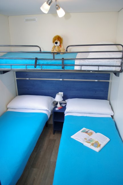 Camera con letti singoli e letto a castello, copriletto azzurri e un peluche sul letto superiore.