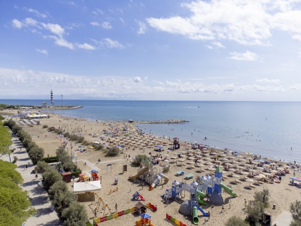 Spiaggia con ombrelloni e giochi per bambini, mare calmo sullo sfondo.