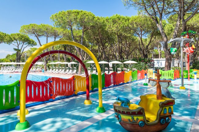 Area giochi acquatica con archi colorati e un piccolo scivolo a forma di barca.
