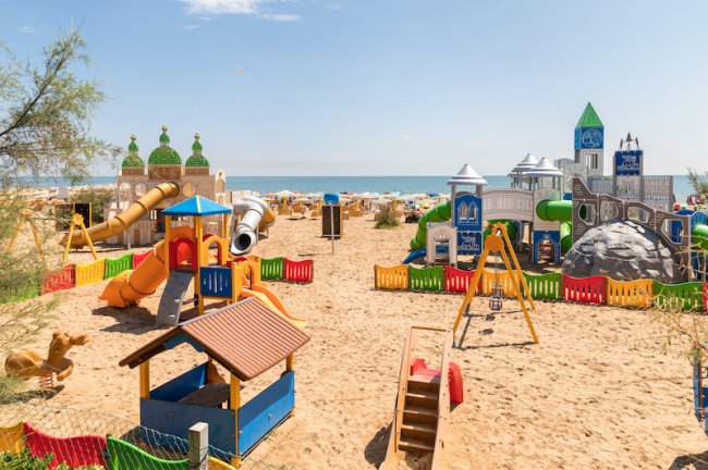 Parco giochi sulla spiaggia con numerosi scivoli colorati e strutture a tema castelli.