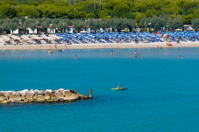 Spiaggia affollata con mare calmo e kayak.