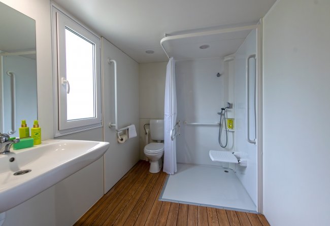 Bagno con doccia accessibile e pavimento in legno.