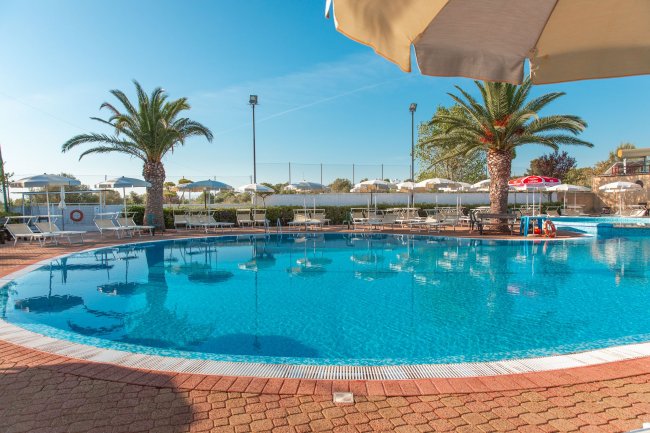 Piscina con palme e lettini sotto un ombrellone.