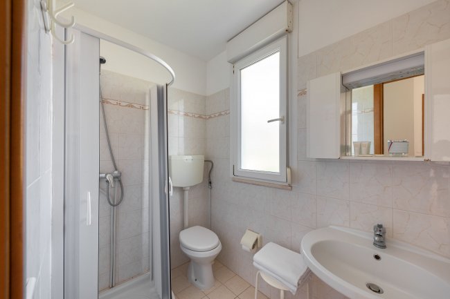 Bagno con doccia, WC e lavabo, finestra accanto.