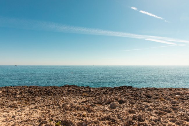 Costa rocciosa e mare calmo sotto un cielo sereno.