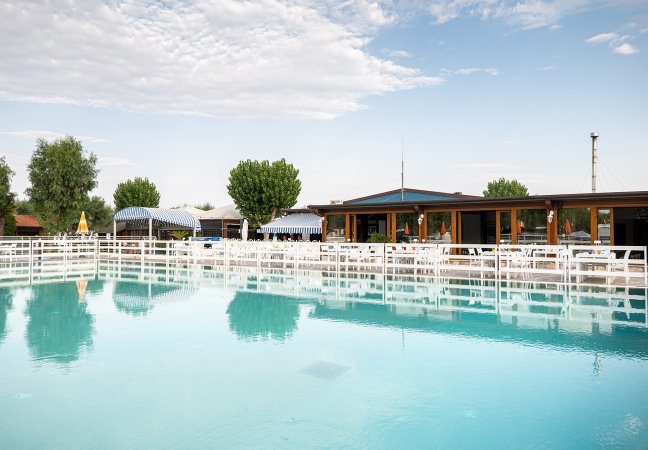 Piscina vuota riflette cielo e ombrelloni.
