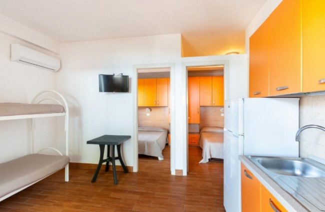 Soggiorno con letti a castello e cucina arancione.