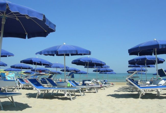 Spiaggia con ombrelloni e sdraio blu sotto il cielo sereno.