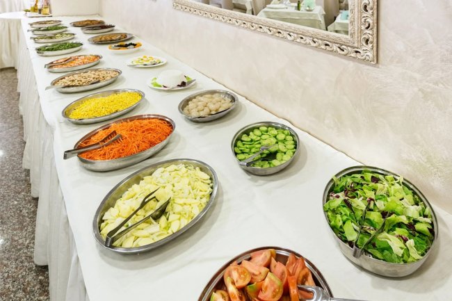 Buffet con insalate e verdure in ciotole metalliche.