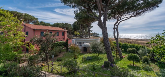 Vista di un edificio rosa, giardino e mare sullo sfondo.