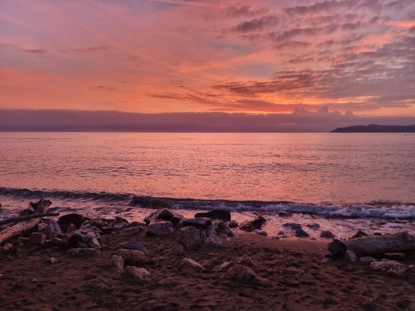 Tramonto rosa sul mare con spiaggia rocciosa.