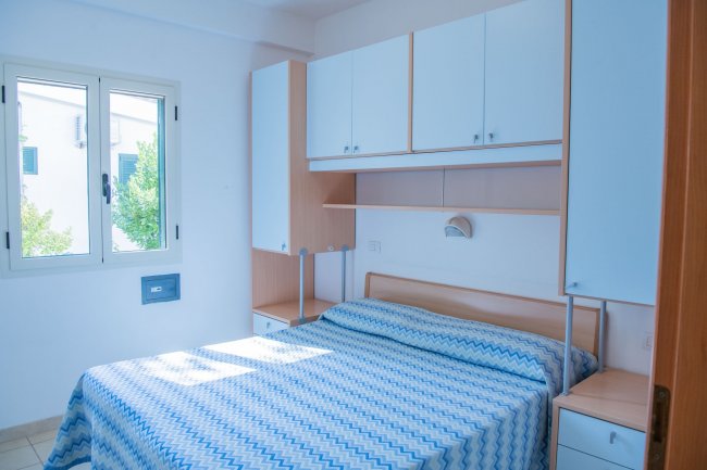 Camera da letto luminosa con letto matrimoniale e parete attrezzata.