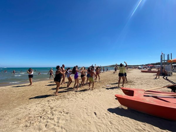 Persone ballano su una spiaggia assolata.