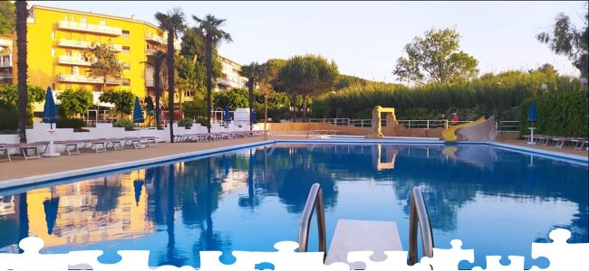 Piscina con scivolo, circondata da palme e lettini.