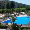 Una piscina circondata da lettini e ombrelloni, con colline verdi sullo sfondo.