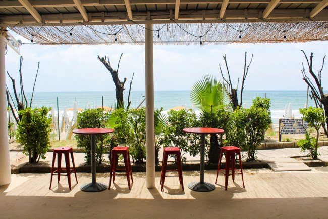 Tavolini rossi fronte mare sotto una tettoia di paglia.