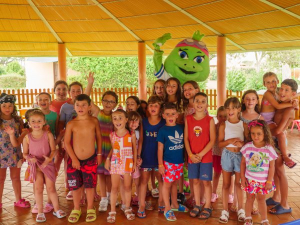 Gruppo di bambini con mascotte verde sorridente.