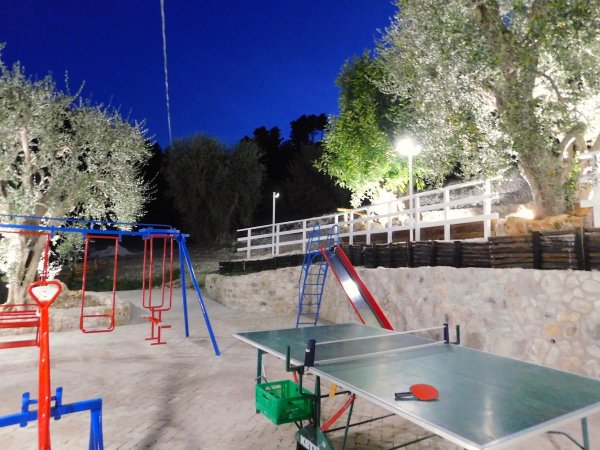 Parco giochi illuminato di sera con altalene e tavolo da ping pong.