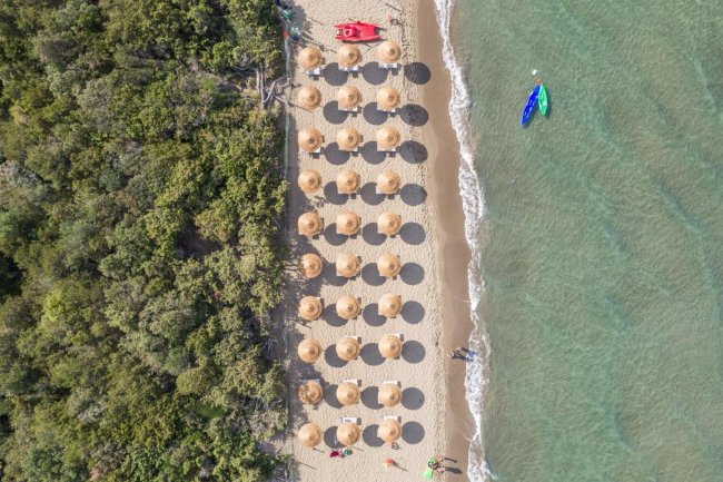 Spiaggia con ombrelloni di paglia visti dall'alto.