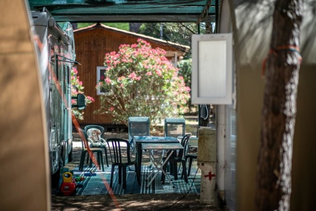 Tavolo da campeggio con sedie, roulotte e fiori sullo sfondo.