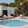 Piccole piscine rotonde con lettini, palme, e una struttura bianca sullo sfondo.