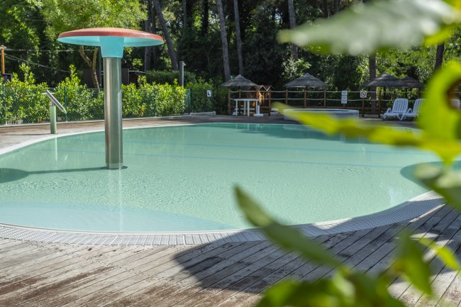 Piscina con ombrello rosso al centro e vegetazione intorno.