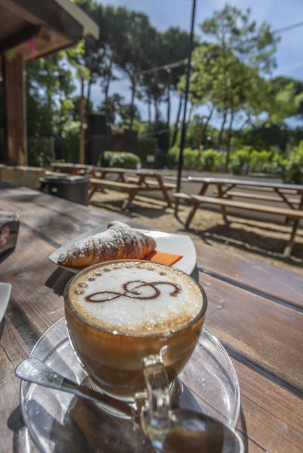 Tavolo all'aperto con cappuccino e cornetto.