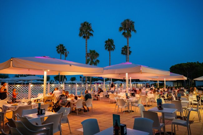Ristorante all'aperto illuminato di sera con palme.