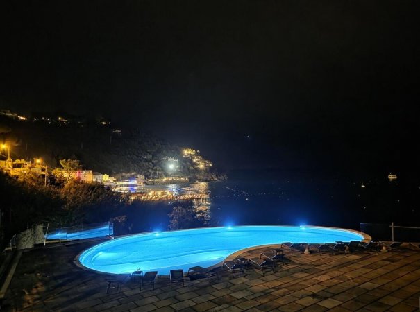 Piscina illuminata di notte con vista sul mare.