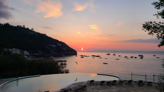 Tramonto sul mare con piscina e sedie a sdraio.