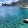 Acqua cristallina con montagne sullo sfondo e una costa rocciosa.