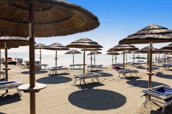 Spiaggia con ombrelloni di paglia e lettini vuoti sotto un cielo limpido.