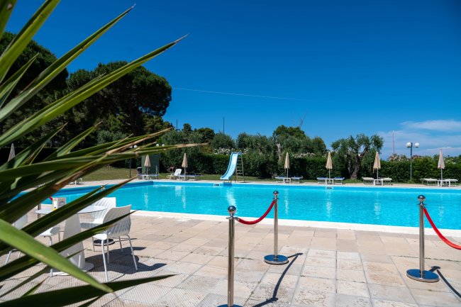 Piscina con scivolo e ombrelloni, cielo blu.