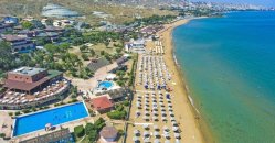 Spiaggia con ombrelloni, mare turchese e un hotel con piscina.
